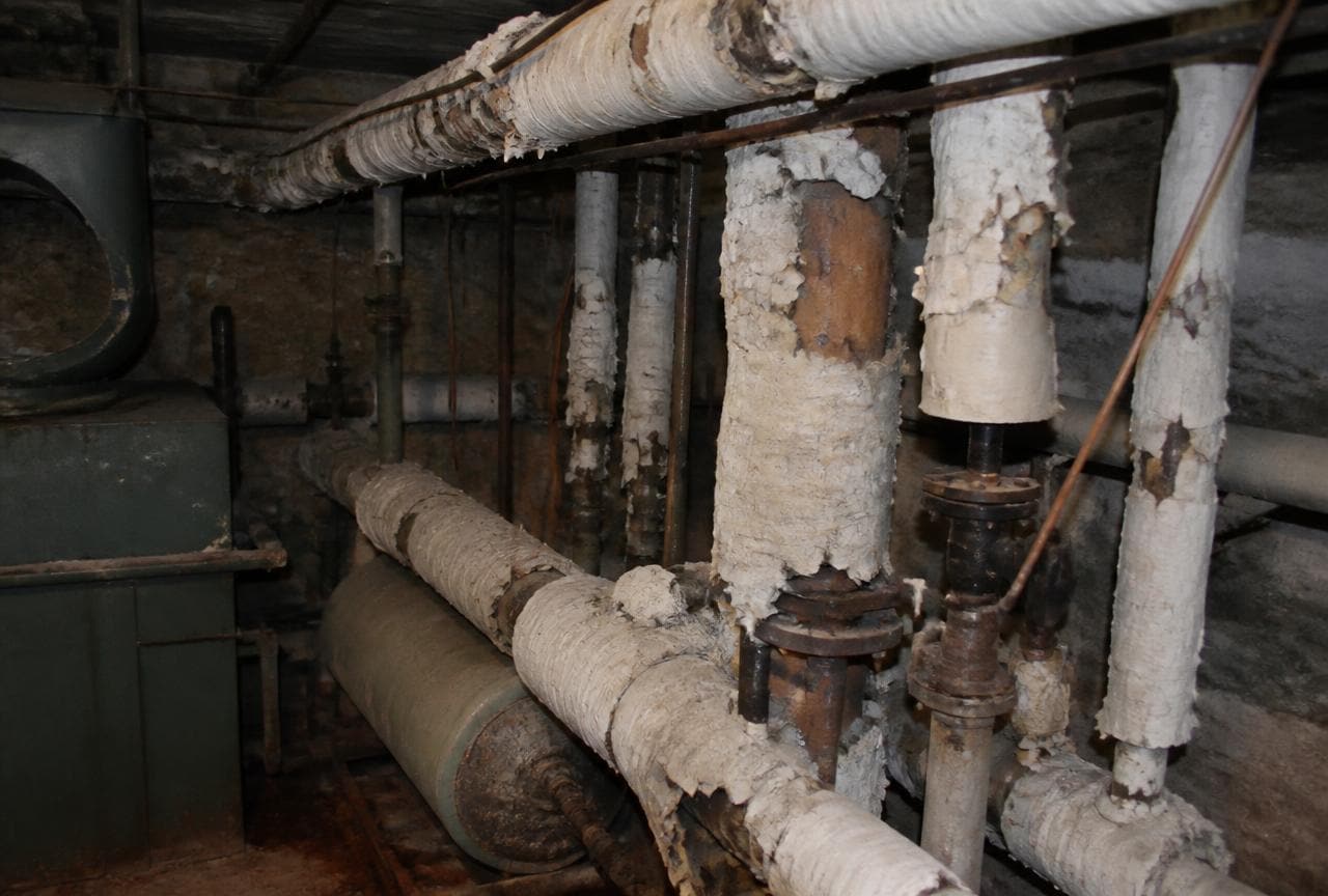 Alte Heizungsrohre im Keller mit weisser, bröckelnder Isoliermasse und offenen Fehlstellen