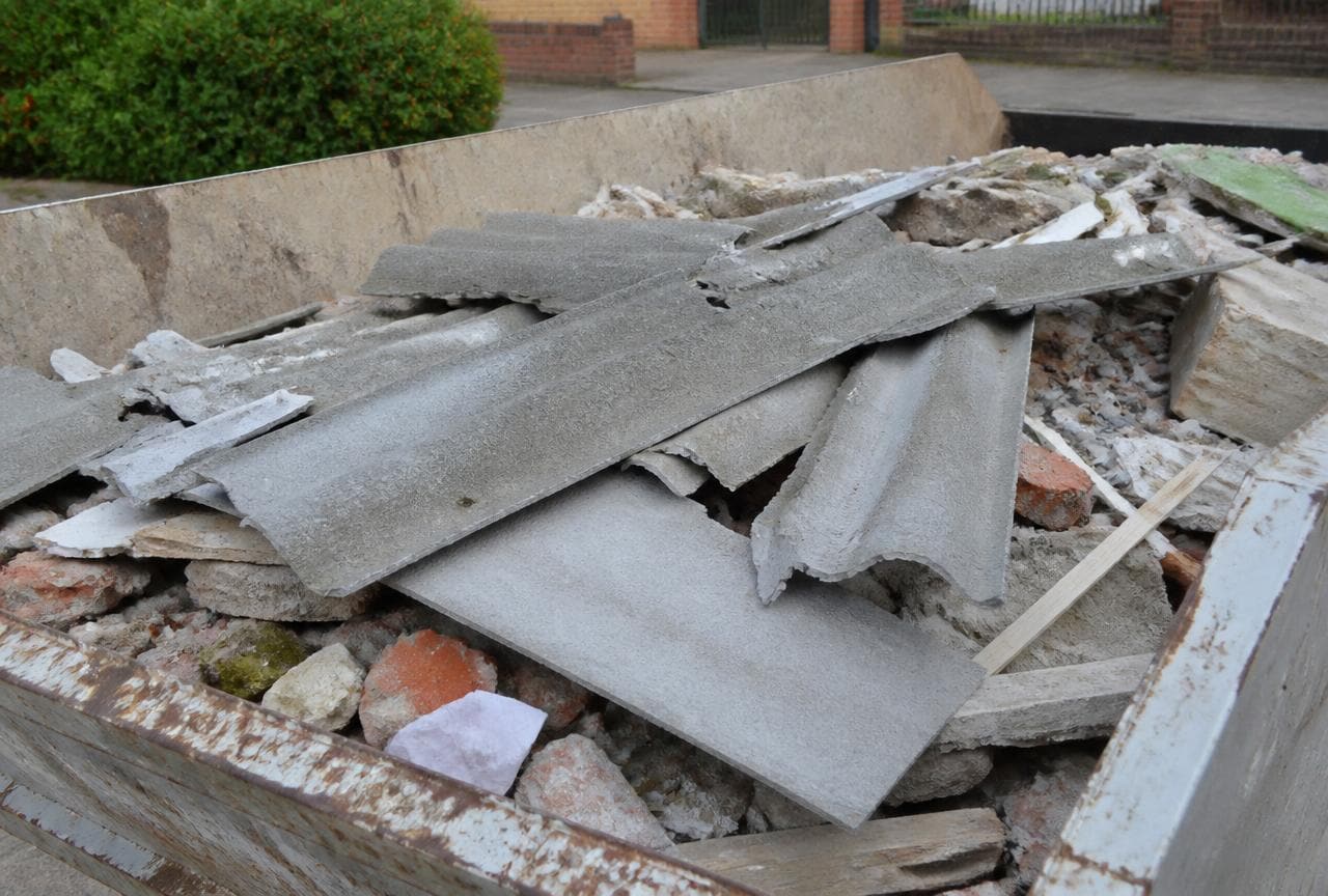 Zerbrochene Faserzementplatten liegen falsch entsorgt in einer Bauschuttmulde