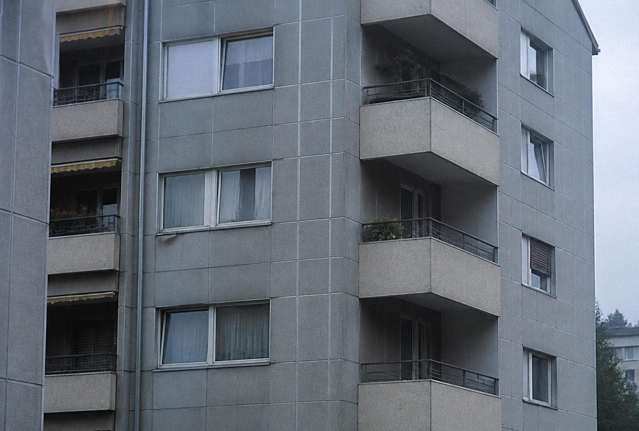 Mehrfamilienhaus aus den 1970er-Jahren mit grauer Faserzement-Fassadenverkleidung und Balkonen