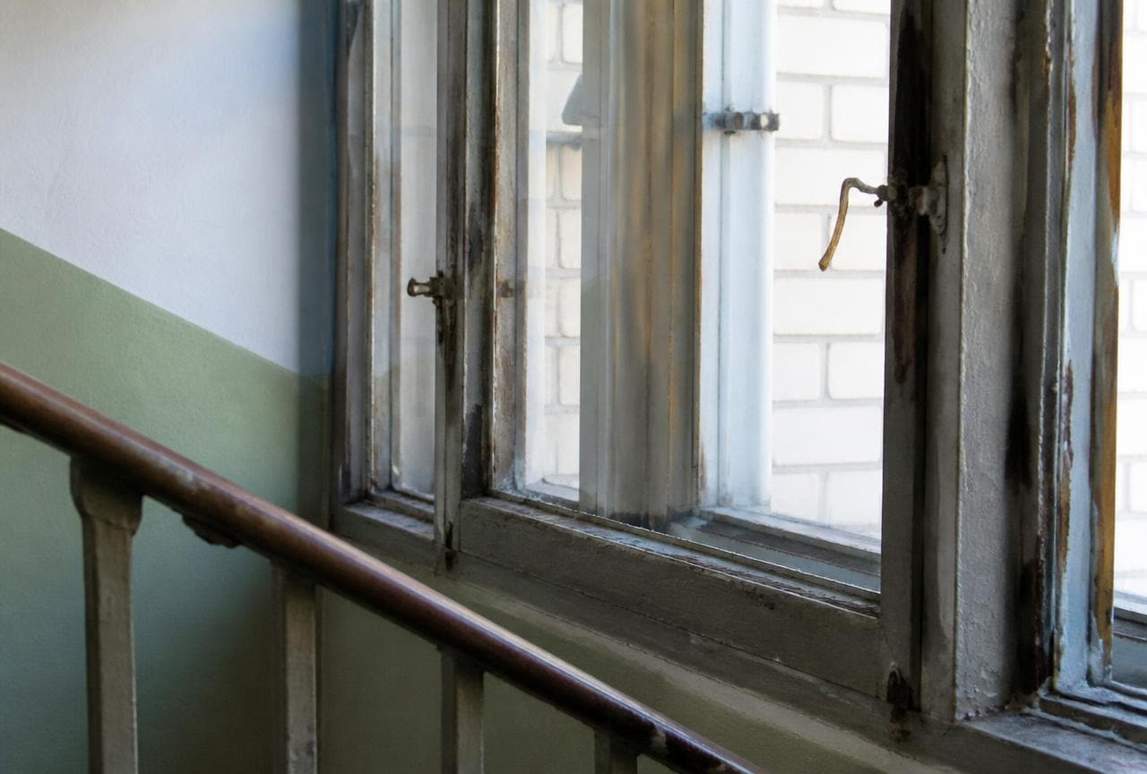 Altes Metallfenster im Treppenhaus mit grauem Kitt und rostigen Beschlägen