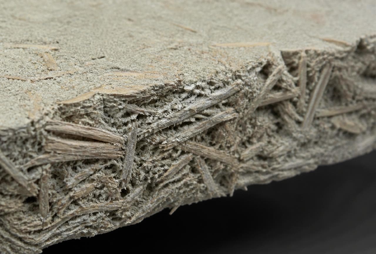 Nahaufnahme der Bruchkante einer Holzwolle-Leichtbauplatte mit strohartigen Fasern im Zement