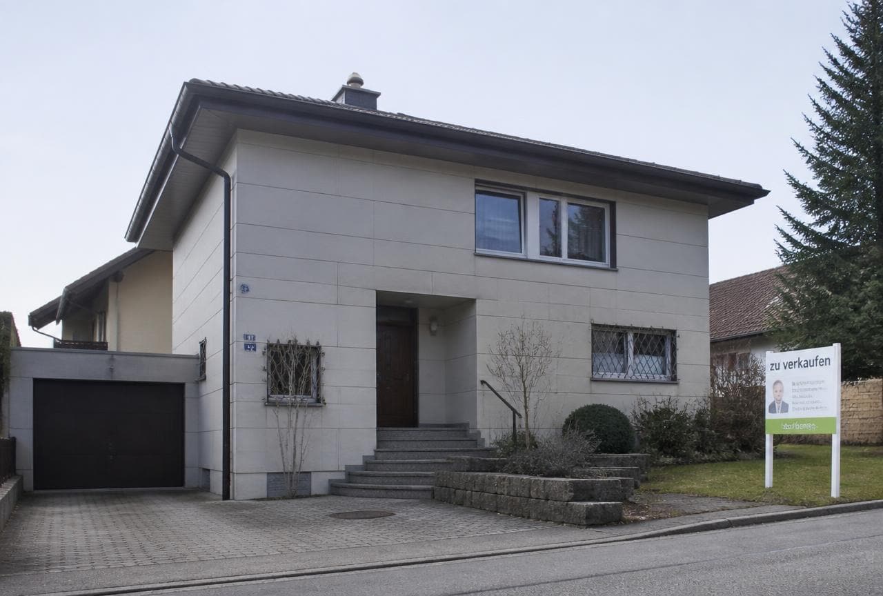 Schweizer Einfamilienhaus aus den 1970er-Jahren mit Faserzementplatten an der Fassade und Verkaufsschild