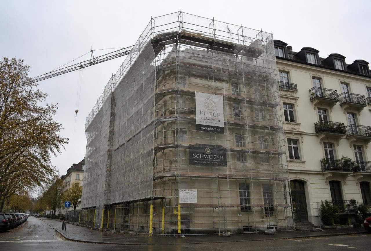 Eingerüstetes älteres Mehrfamilienhaus mit Schutznetz während einer Sanierung
