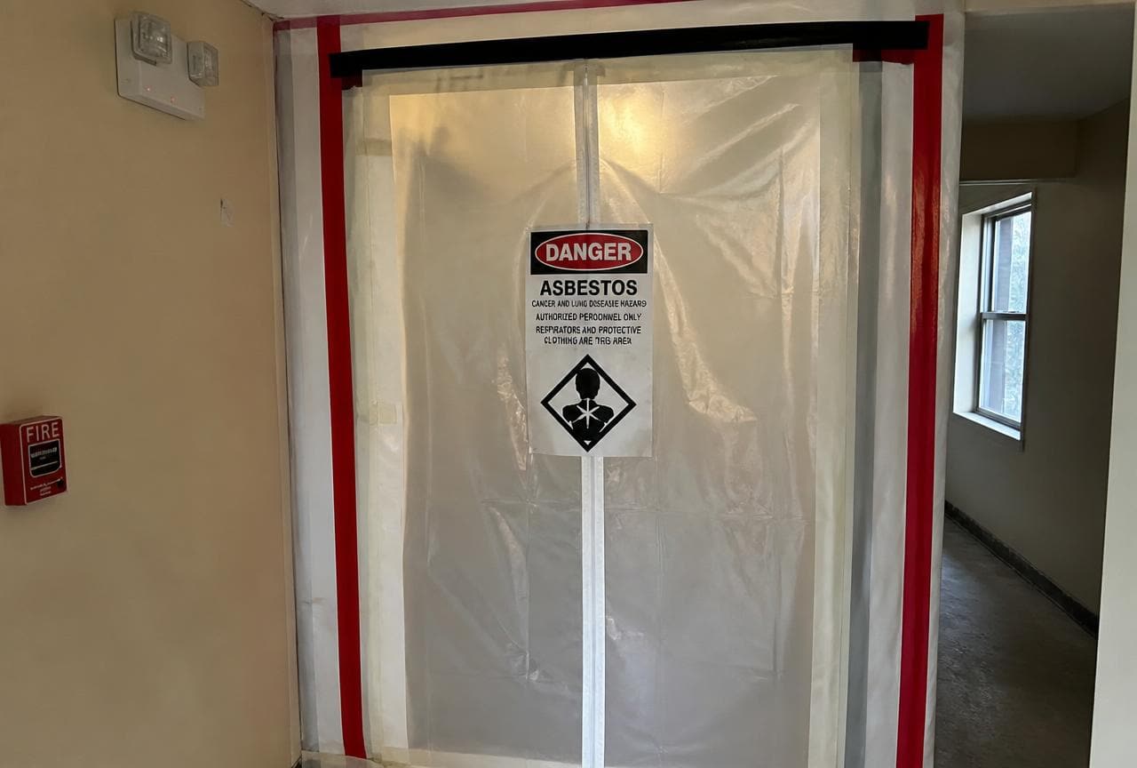 Mit Folie abgeschotteter Zugang zu einer Asbest-Sanierungszone mit Warnschild