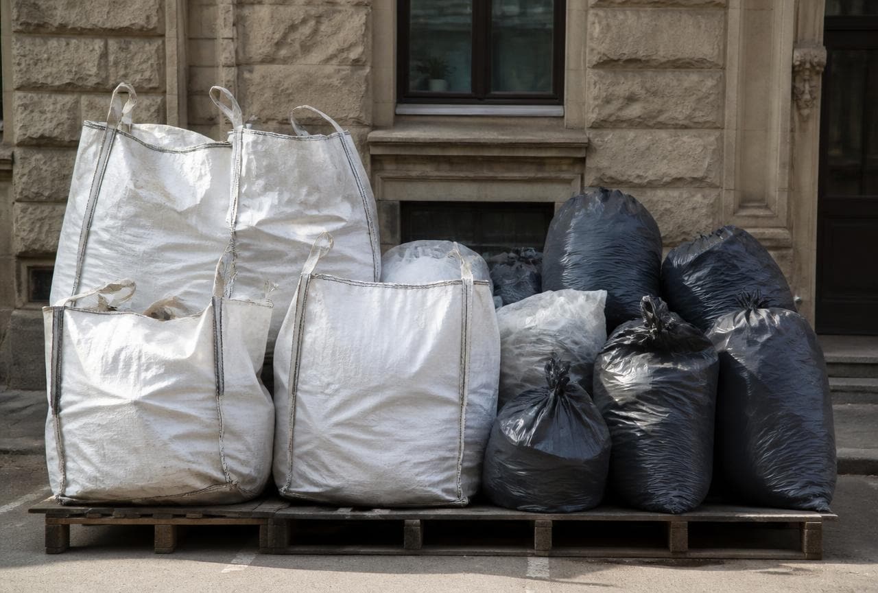 Verschlossene Big Bags und Entsorgungssäcke mit Bauschutt auf einer Palette vor einem Altbau