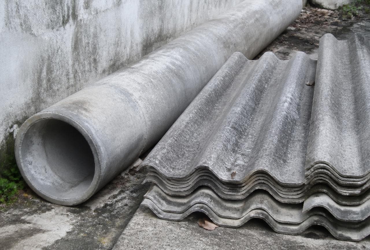 Graue Asbestzement-Wellplatten und ein dickwandiges Faserzementrohr an einer Aussenwand