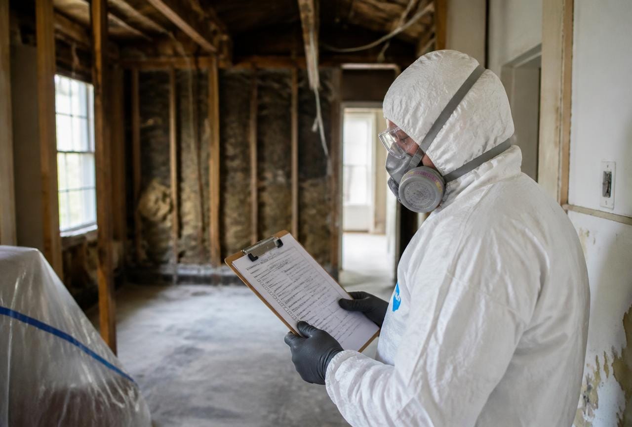 Fachperson im Schutzanzug mit Atemschutzmaske prüft eine Sicherheits-Checkliste auf der Baustelle